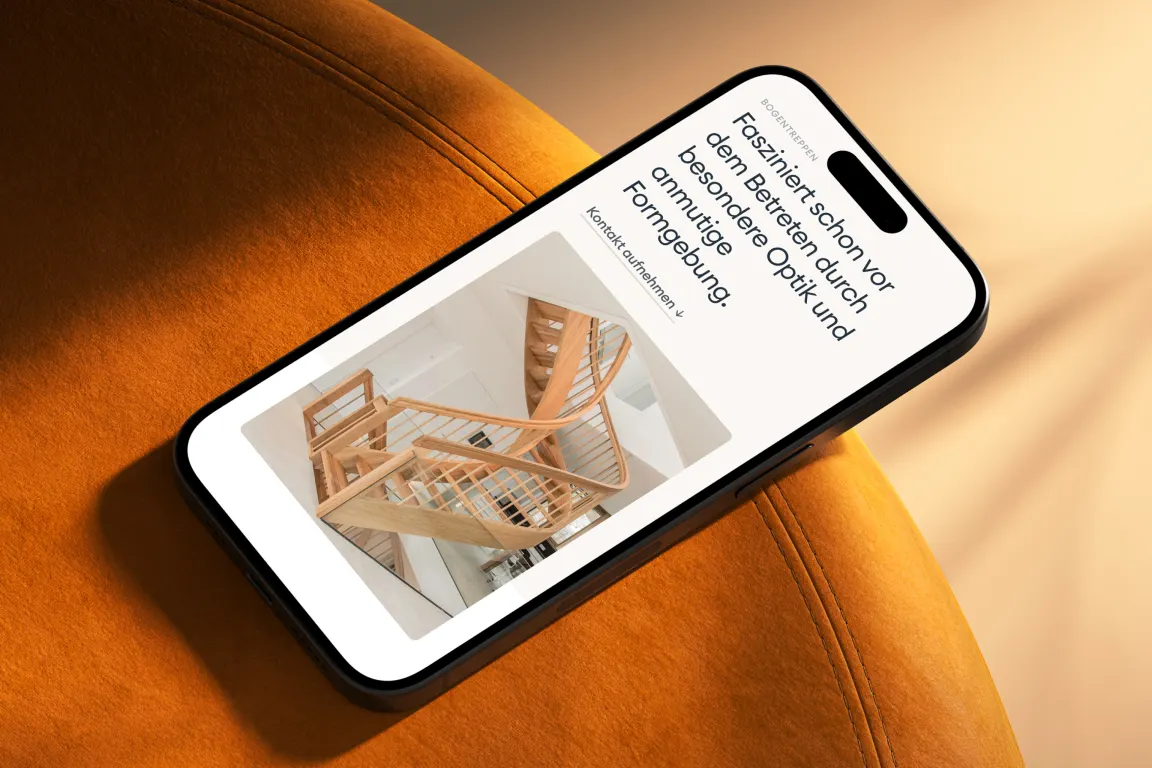 Ballert-Website auf einem iPhone, das auf einem orangefarbenen Polster liegt, mit einer Aufnahme einer geschwungenen Holztreppe