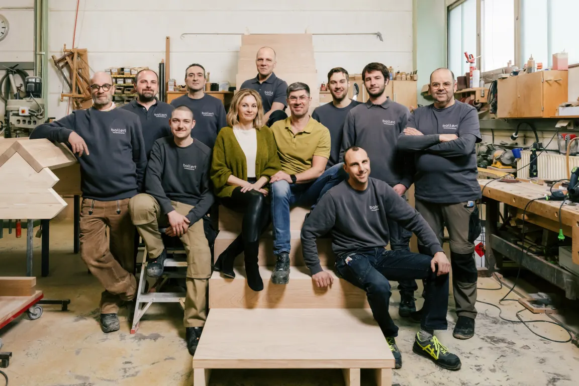 Elf Mitarbeitende der Ballert Holzmanufaktur zwischen Werkbänken in der Schreinerei